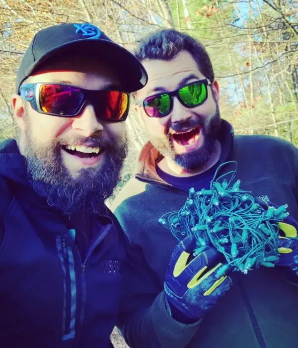 Two men smiling holding a bundle of lights
